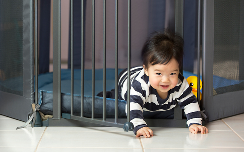 Asian toddler boy open the play pen door, escaping, crawling out happily.